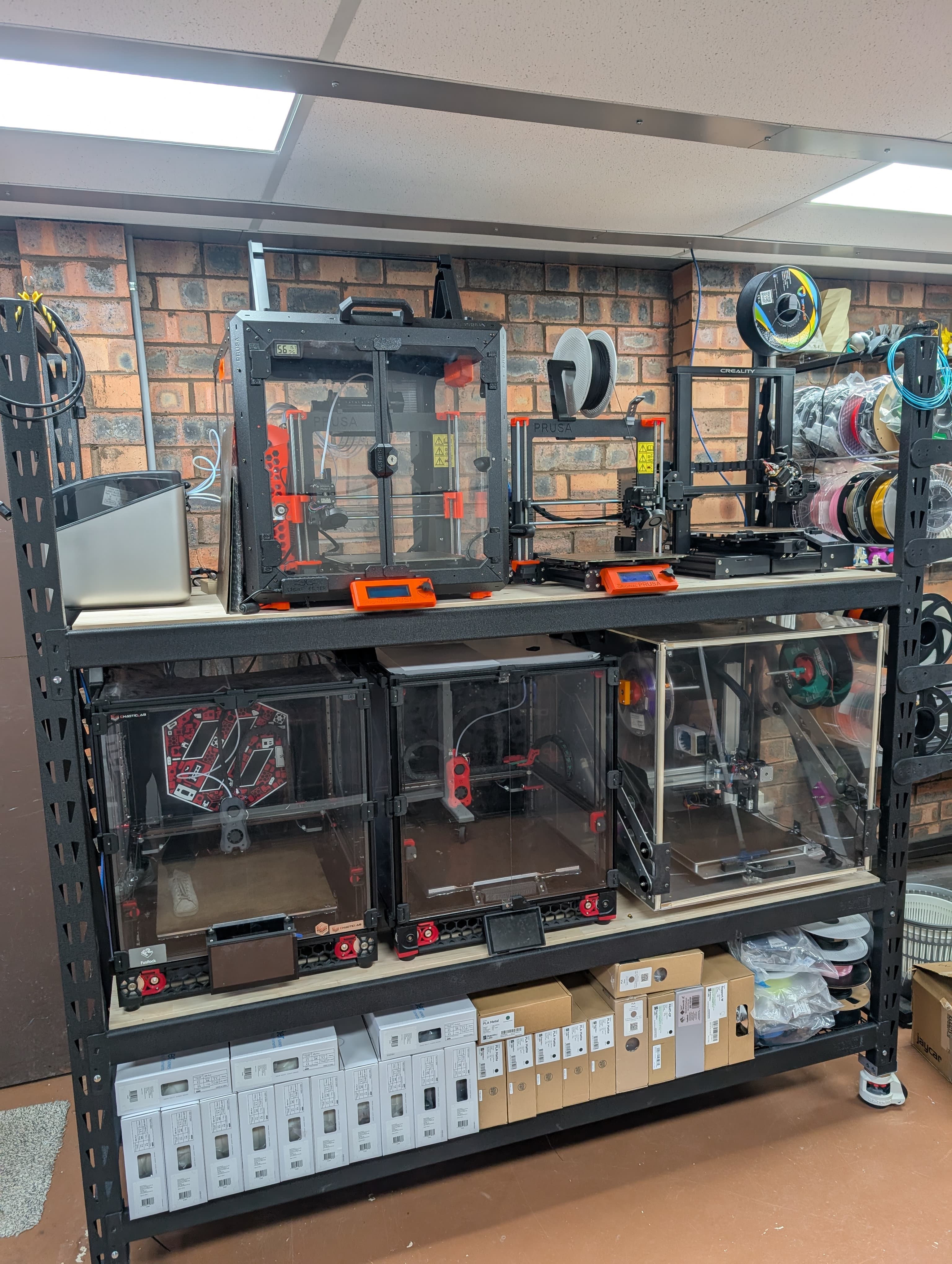 Workshop installation with multiple enclosed FDM printers and a robotic arm mounted above the work area