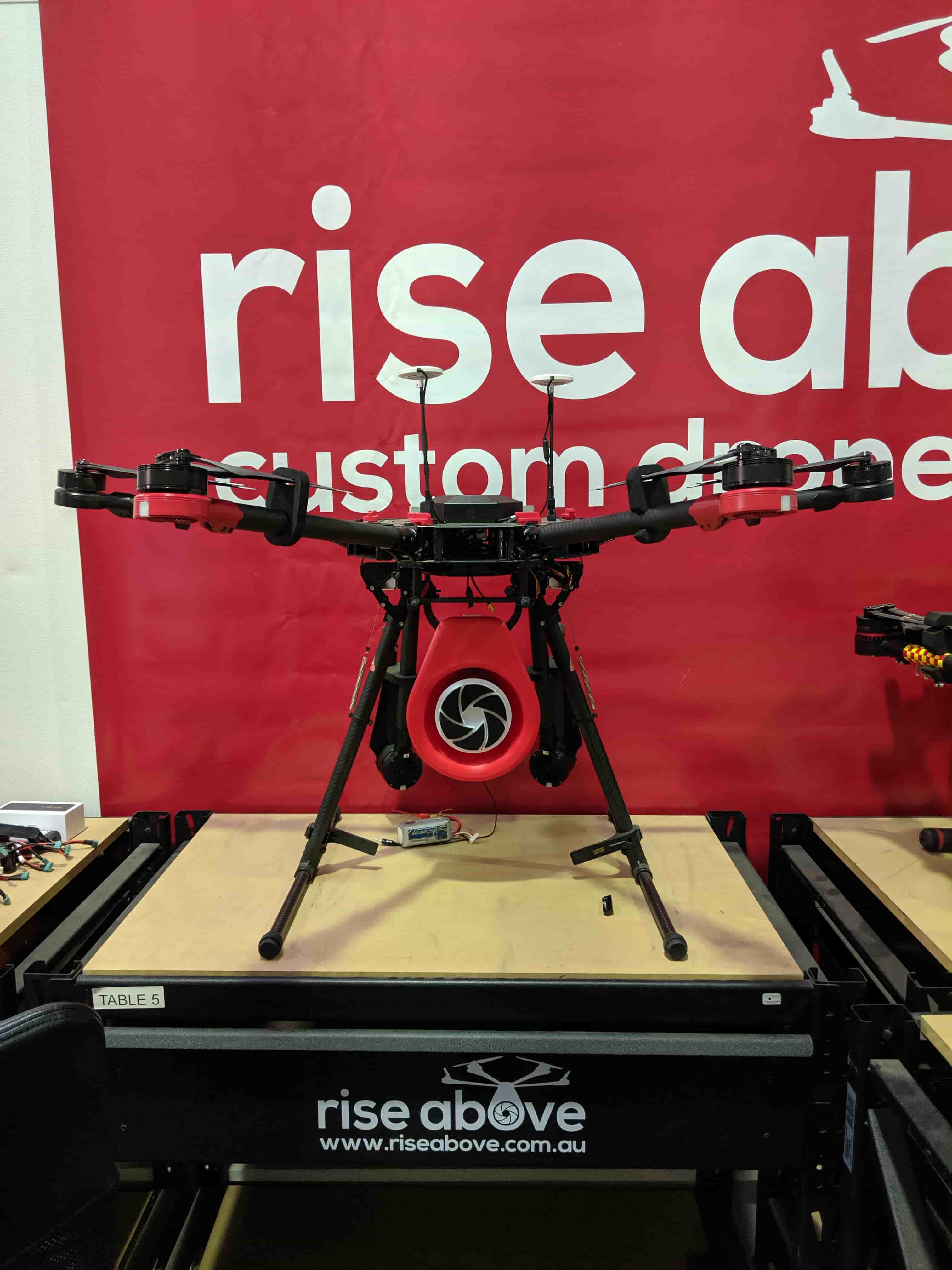Front view of the integrated drone and megaphone payload against a Rise Above display wall