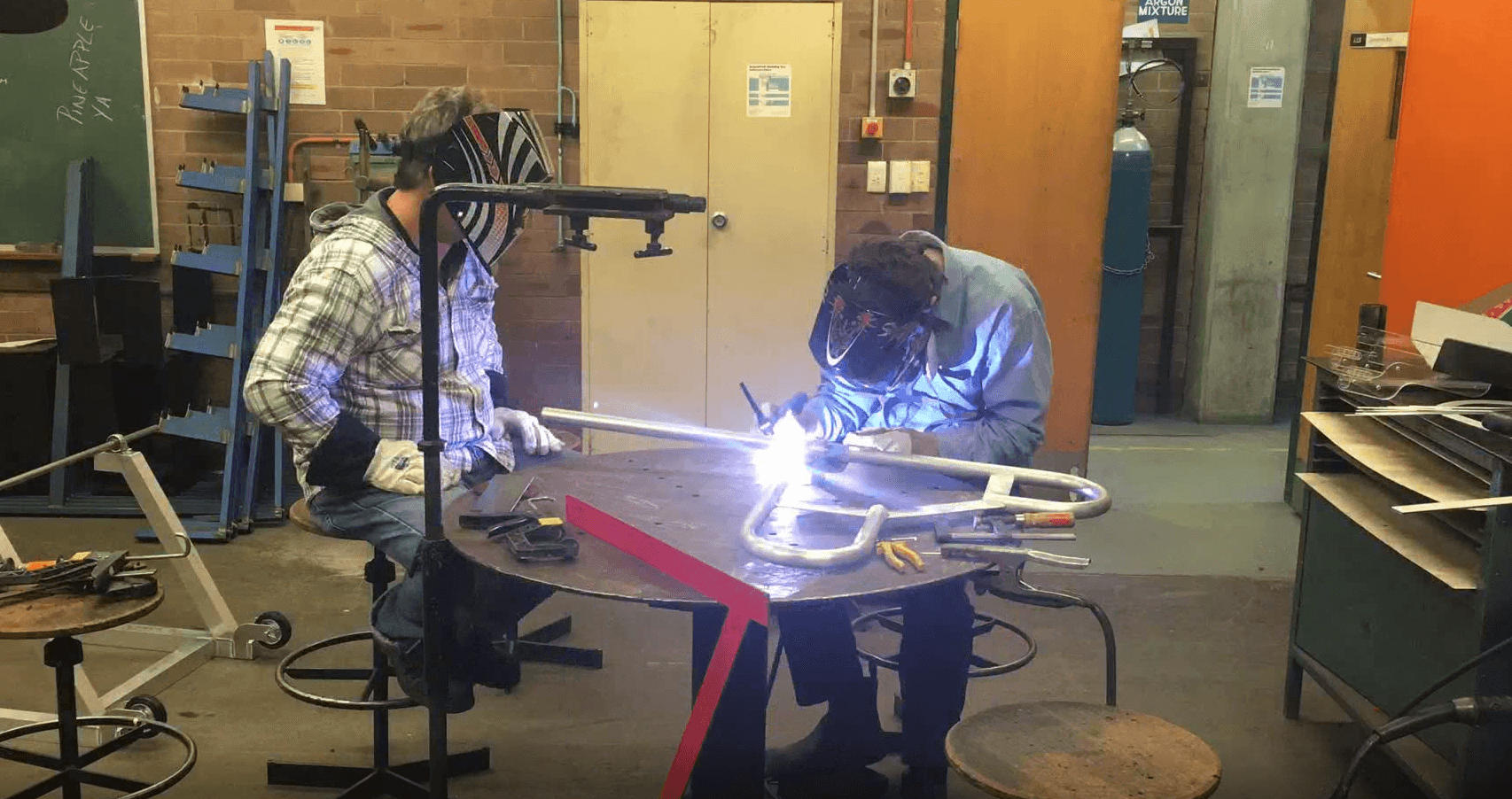 Fabrication team welding a tubular steel frame at the workshop bench